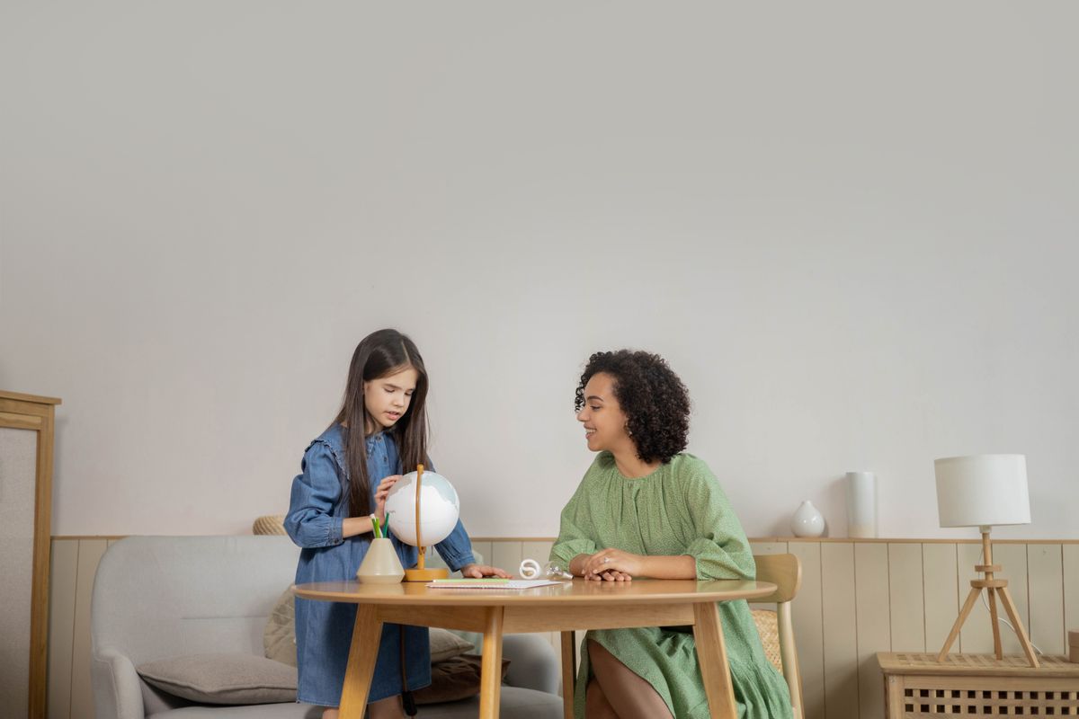 A teacher and student engage in a geography lesson with a globe in a cozy indoor setting.