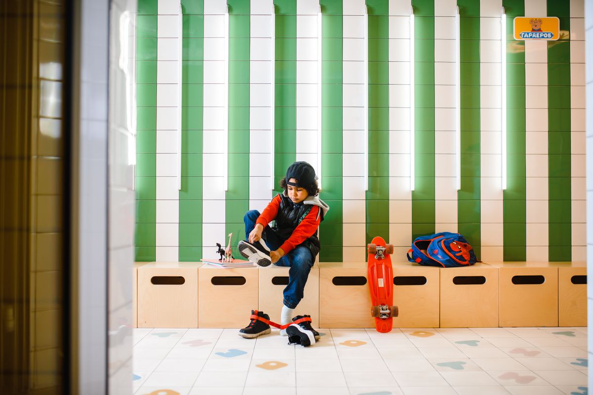 Young child in a locker room tying shoes surrounded by skateboard and backpack, ready for fun and activity. - Photo by Anastasia  Shuraeva on Pexels