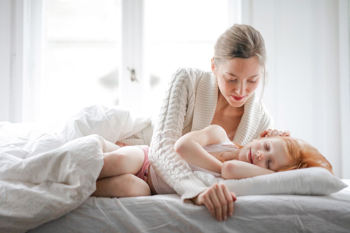 Low angle of joyful young woman in casual clothes lying and caressing small girl sleeping in soft bed in light modern bedroom at home in daytime - Photo by Andrea Piacquadio on Pexels