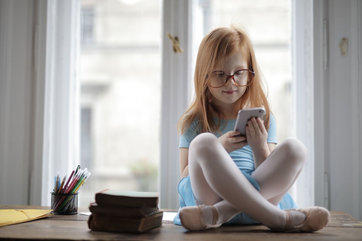 Jolie fille aux cheveux roux utilisant un smartphone assise sur un rebord de fenêtre à l'intérieur. - Photo par Andrea Piacquadio sur Pexels