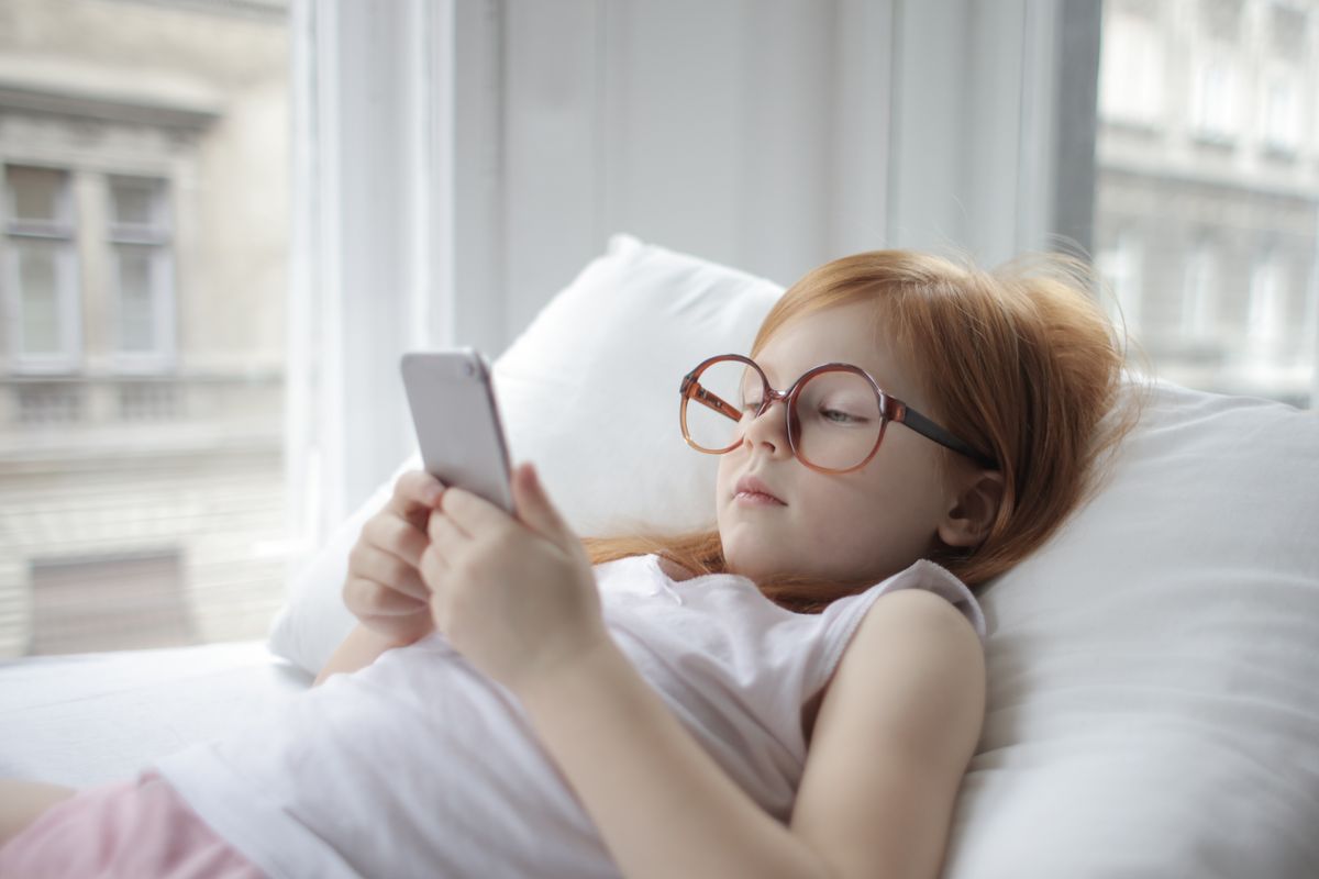 Girl relaxing indoors with a smartphone, showcasing modern childhood leisure. - Photo by Andrea Piacquadio on Pexels