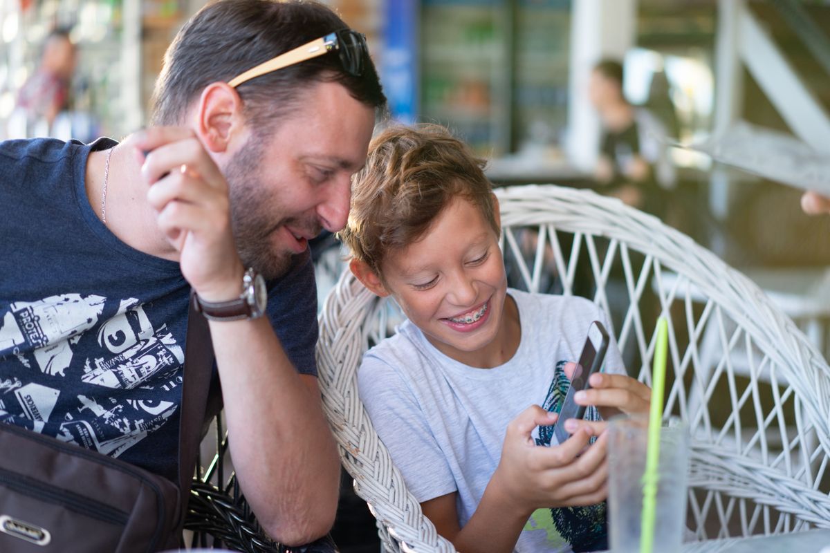 Father and son bonding over a smartphone, sharing a joyful moment in a cozy cafe. - Photo by Atlantic Ambience on Pexels