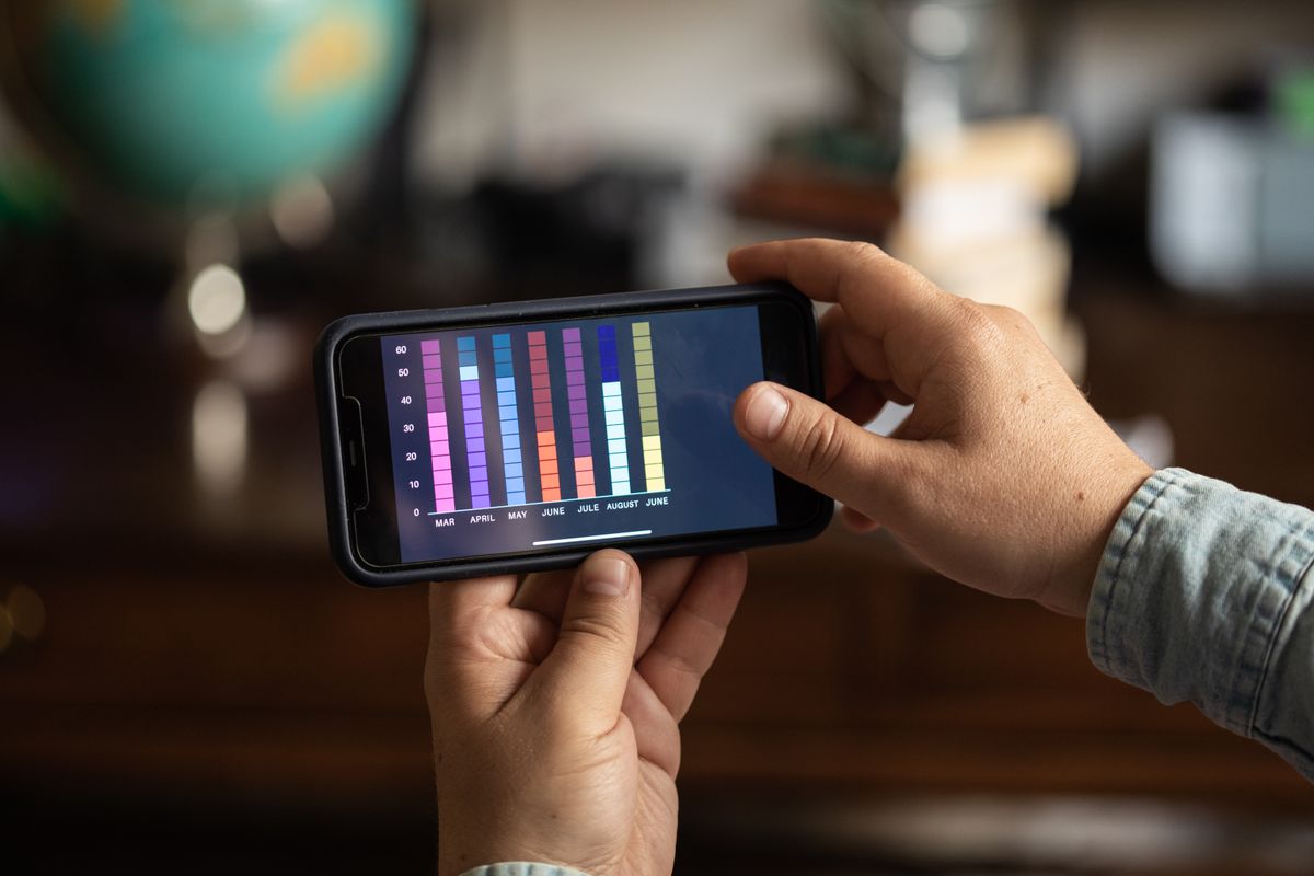 Nahaufnahme von Händen, die ein Smartphone halten und ein buntes Balkendiagramm anzeigen. Perfekt für Business- und Technologiethemen.