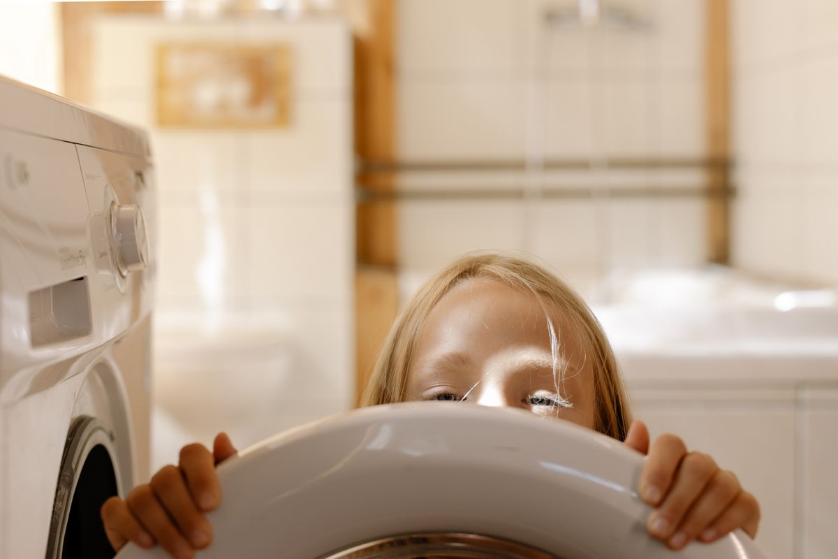 Una ragazza fa capolino dalla lavatrice e aiuta con i lavori di lavanderia in casa. - Foto di cottonbro studio su Pexels