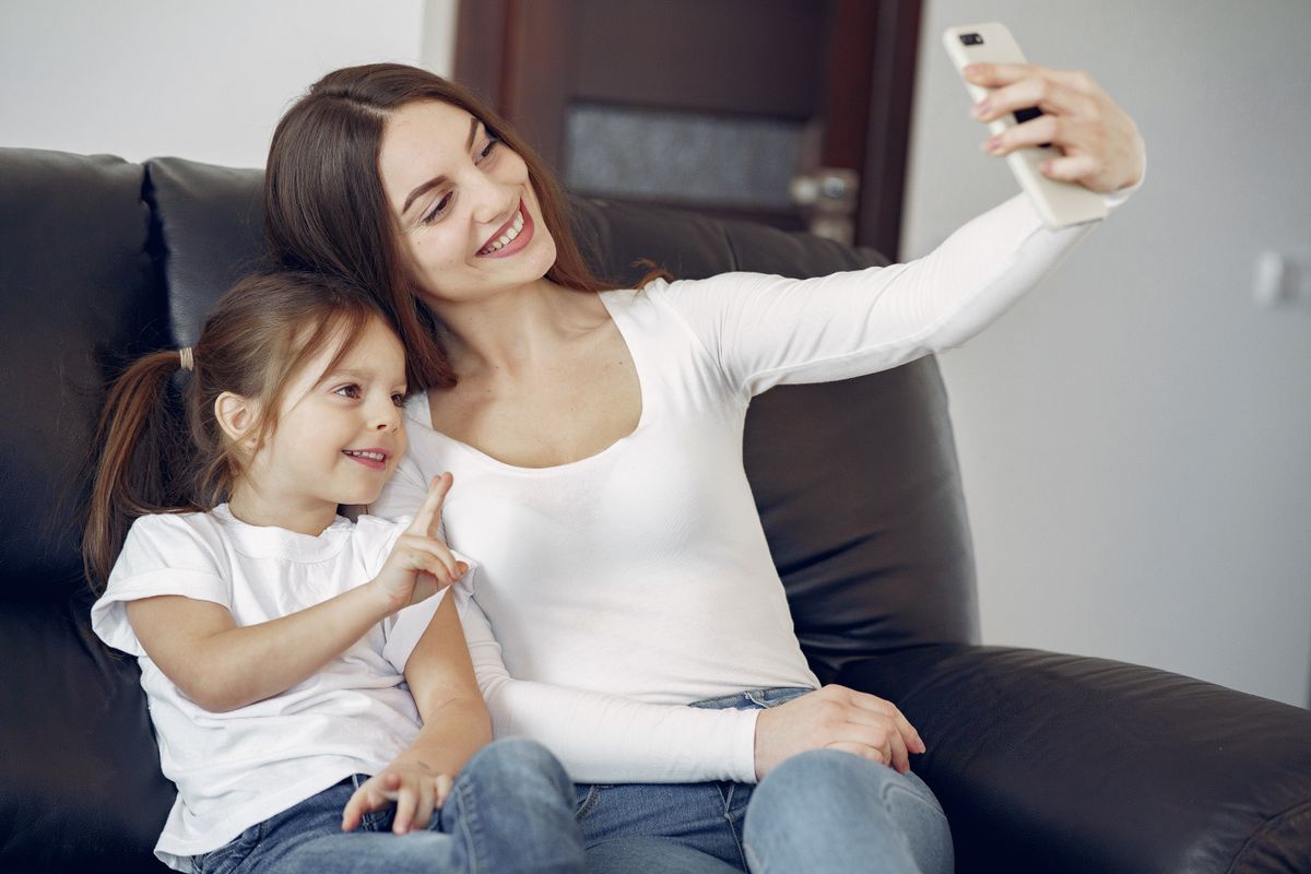 Delighted mother and daughter in casual wear sitting on sofa and taking selfie while resting in contemporary living room during daytime - Photo by Gustavo Fring on Pexels