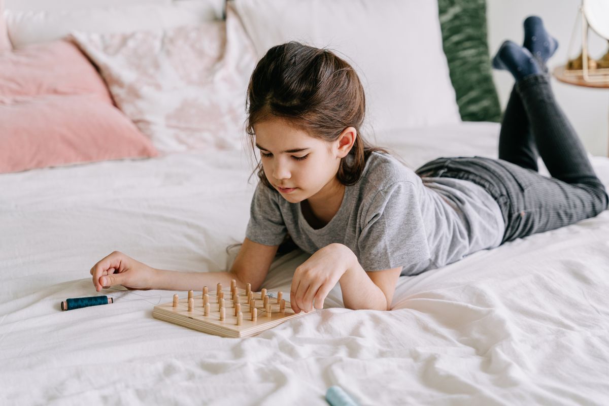 Ein junges Mädchen, das auf einem Bett liegt, vertieft sich in eine achtsame Geoboard-Aktivität im Innenbereich. - Foto von Ivan S auf Pexels