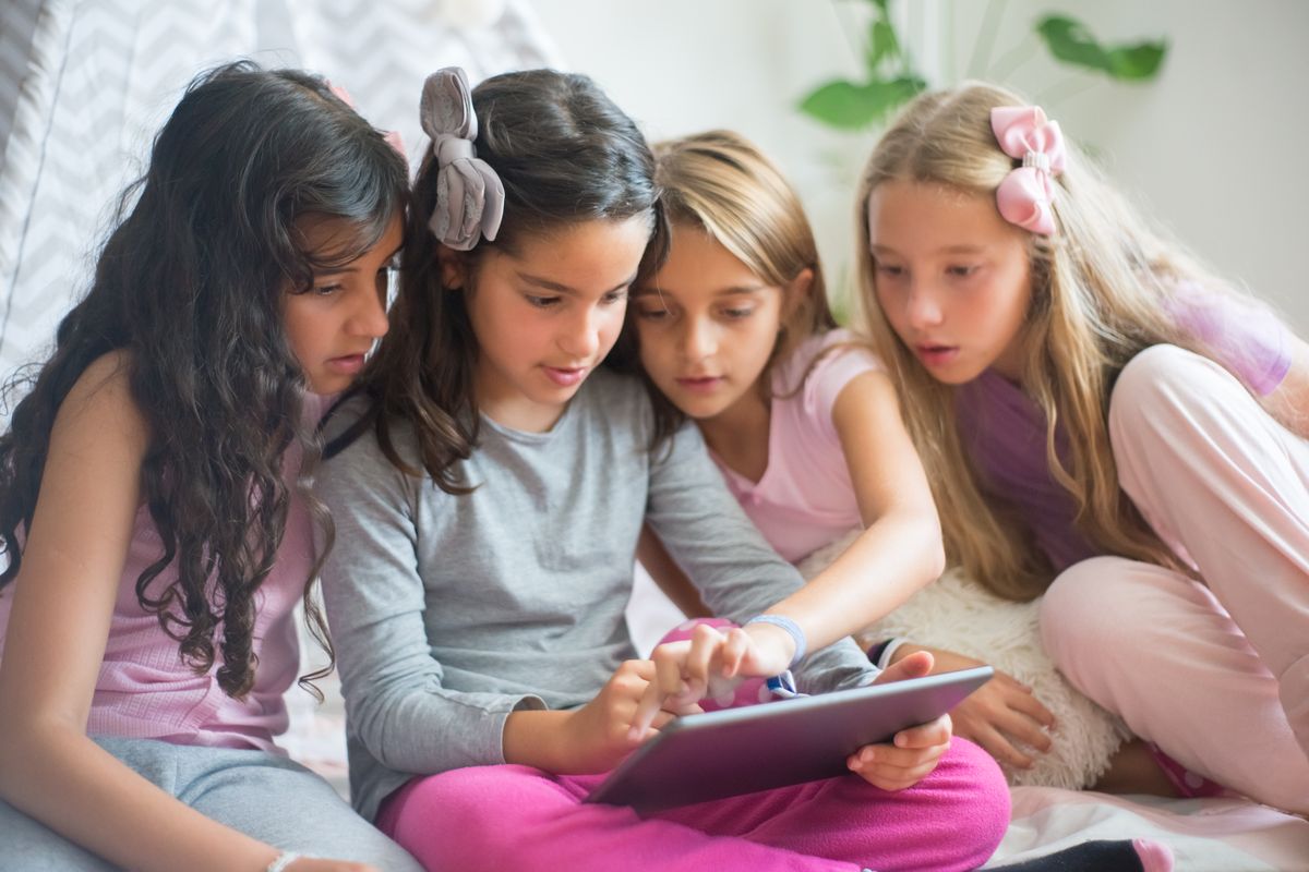 Four young girls sitting together, engaged and focused on a tablet in a cozy indoor setting. - Photo by Kampus Production on Pexels
