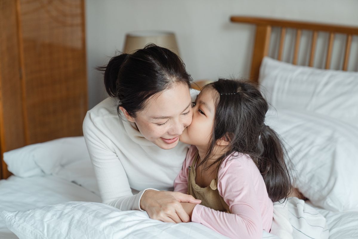Süßes asiatisches Mädchen küsst sich auf die Wange und freundet sich mit einer lächelnden jungen Mutter an, während es morgens im Komfortbett liegt und gemeinsam die freie Zeit genießt – Foto von Ketut Subiyanto auf Pexels