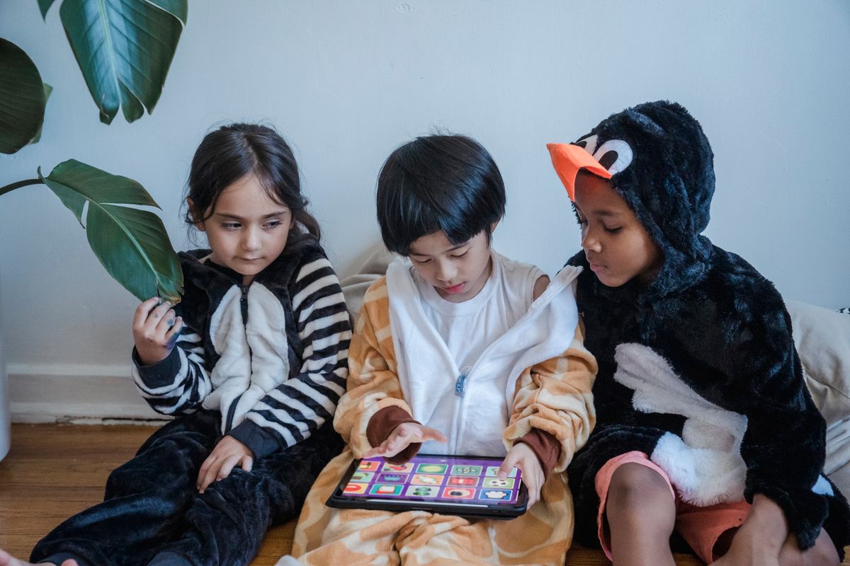 Kids in animal onesies playing on a tablet indoors, enjoying leisure time. - Photo by Liliana Drew on Pexels