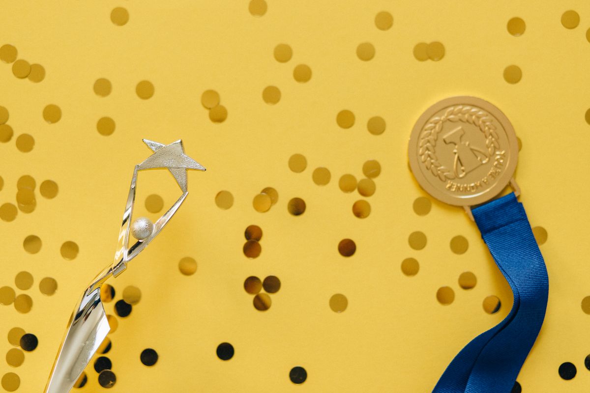 Golden medal and silver trophy with confetti on yellow surface, celebrating achievement. - Photo by Nataliya Vaitkevich on Pexels