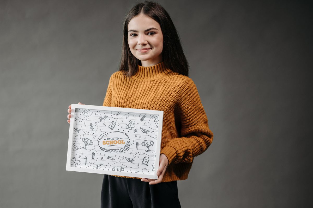 A smiling teenage girl holds a back-to-school poster in a studio setting. - Photo by Pavel Danilyuk on Pexels