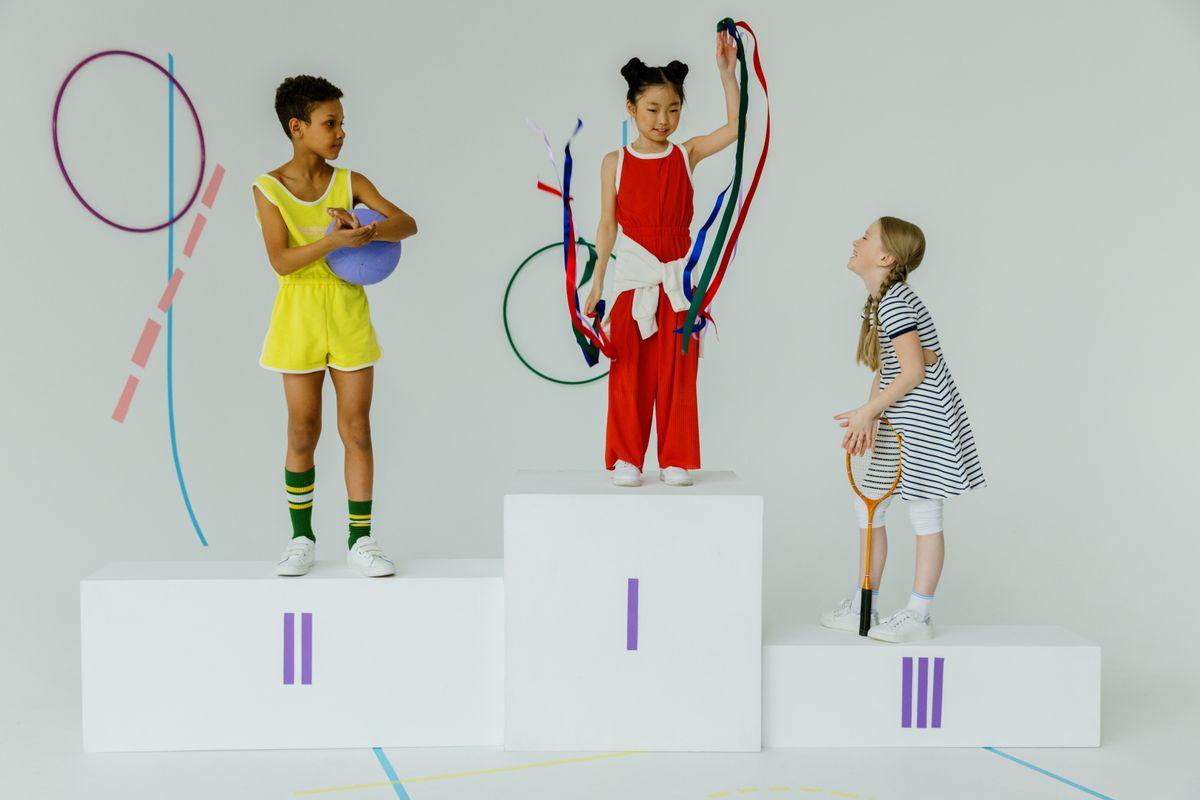 Three happy children celebrating on a gymnastics podium with equipment.