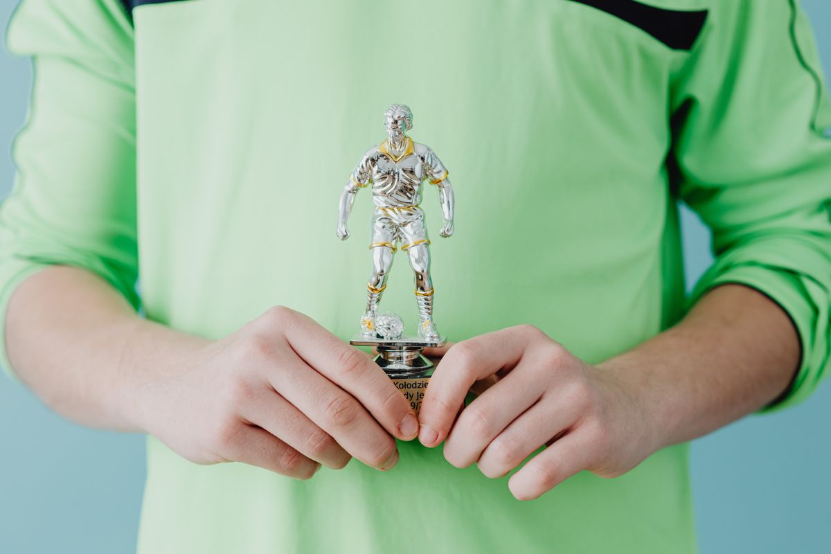 A person holding a silver soccer trophy against a blue background. - Photo by www.kaboompics.com on Pexels